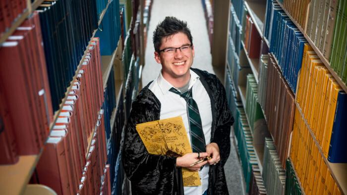 An instructor in wizard apparel stands between isles of books